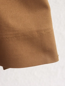 Detailed close-up of khaki twill fabric texture and high-quality stitching on short trench coat