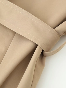 Detailed close-up of khaki trench coat fabric texture with fine double stitching and belt