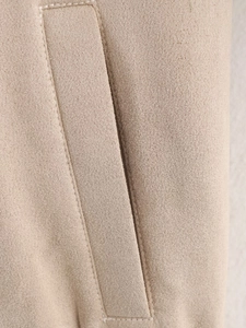 Detail view of the side pocket on a beige suede jacket showing clean stitching and texture