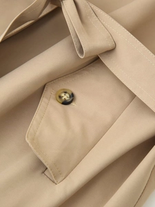 Detailed macro view of khaki cotton trench coat pocket with tortoise button and stitching