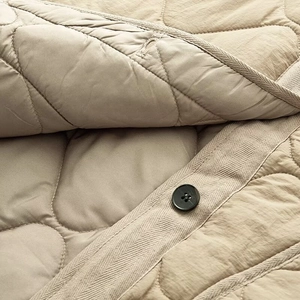 Detail of khaki quilted jacket with diamond patterns and black button closure