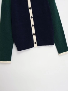 Detail of color-block knit cardigan with navy body, green sleeves and white piping