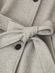 Detailed shot of beige wool coat featuring textured fabric, tie belt and wooden button