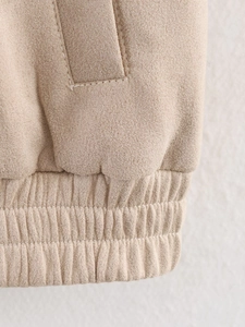 Detailed close-up of ribbed hem and pocket stitching on apricot suede jacket fabric