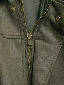 Gros plan sur le zip doré et le bouton pression de la veste bomber en daim olive