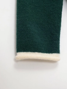 Detail of dark green knit sweater with contrast cream rolled edge and soft wool texture