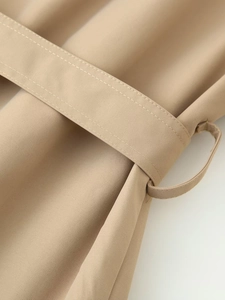 Detail of khaki twill fabric texture and neat stitching on the belted waist of the trench coat