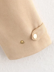 Detail of beige suede jacket sleeve featuring decorative strap and gold metal snap buttons