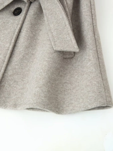 Detailed macro view of soft oatmeal wool texture and black button on a belted coat
