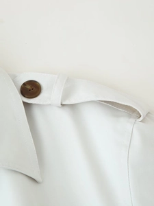Detail of off-white trench coat showing shoulder strap and high-quality twill fabric texture
