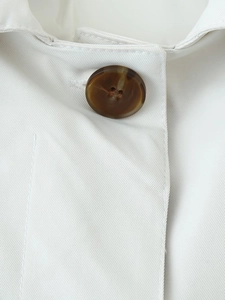 Detailed close-up of a tortoiseshell button on white twill fabric trench coat