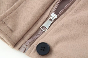 Détail du zip en métal argenté et bouton noir sur une veste en laine courte de couleur camel