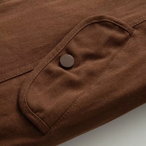 Detail of a brown twill canvas jacket featuring a flap pocket with a dark button closure