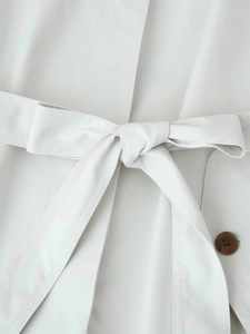 Close-up of belted waist on cream short trench coat with tortoiseshell button detail