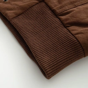 Detailed macro shot of dark brown heavy canvas jacket with high-density ribbed cuff texture