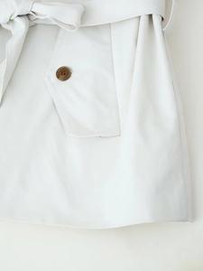 Close-up of beige twill trench coat fabric with a belted waist and buttoned pocket detail