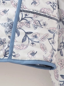 Detailed close-up of blue floral quilted jacket with diamond stitching and contrast piping