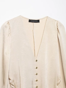 Detail of champagne satin shirt featuring pleated texture, V-neck, and gold button accents