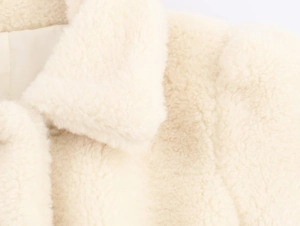Detail of soft cream faux fur texture and lapel design on winter coat with belt