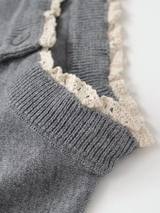Detail von grauem Strickstoff mit zarter beiger Spitze und passendem mattem Knopf