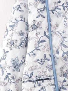 Detail of white quilted jacket featuring navy floral print and blue woven piping trim