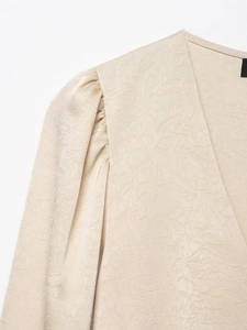 Detail of beige crinkled satin blouse featuring a deep V-neck and puffed pleated sleeves