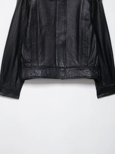 Gros plan sur la texture du cuir grainé noir et les coutures d'un blouson aviateur vintage
