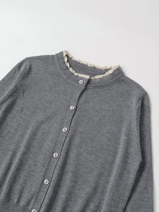 Details der grauen Strickjacke mit zartem Spitzenkragen und glänzenden weißen Knöpfen