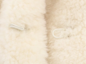 Detail of soft cream faux fur texture with delicate loop fastener closure on coat