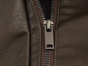 Macro shot of gun-black metal zipper and premium faux suede texture on a dark brown jacket