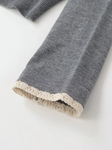 Detailaufnahme grauer Strickärmel mit eleganter weißer Spitzenborte und Textur