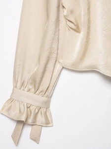 Detailed close-up of champagne blouse with pleated fabric texture and ruffled tied cuffs