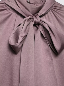 Détail du col d'une chemise en satin avec nœud rose et finition texture sergée