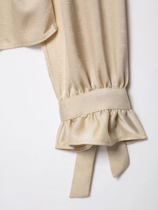 Detail of elegant champagne satin blouse sleeve featuring ruffles and chic tie ribbons