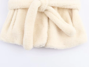 Detail shot of a cream faux fur coat featuring a soft textured belt tied at the waist