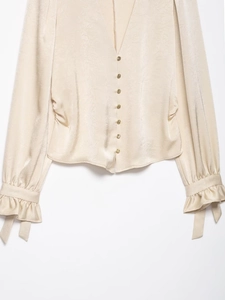 Detail of champagne satin shirt with V-neck, golden buttons and ruffled cuffs decoration