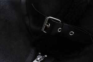 Detail of black faux fur jacket with leather buckle strap and silver metallic hardware