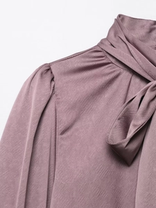 Détail du chemisier en satin avec élégant nœud au col haut et épaules plissées