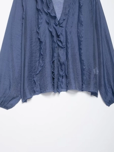 Detail of dark blue crinkled fabric and ruffle trim on a V-neck buttoned blouse