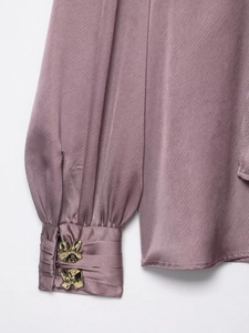 Détail de la manchette de chemise en satin rose avec boutons dorés en forme de nœud