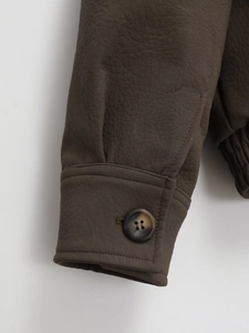 Detailed close-up of dark brown faux leather jacket cuff with tortoise button and elastic hem