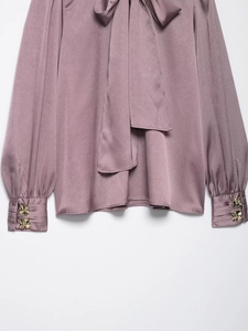 Détail de chemise en satin gris-mauve avec nœud papillon et boutons dorés aux poignets