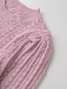Gros plan du pull en tricot rose montrant les motifs de torsades et les détails de dentelle ajourée
