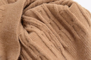 Macro shot of the camel cable knit sweater fabric showing thick rib texture and soft wool feel
