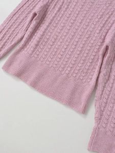 Détail d'un pull en maille ajourée rose montrant la texture au crochet et l'ourlet côtelé