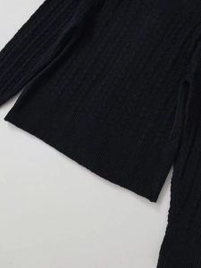 Detail shot of the chunky cable knit texture and ribbed hem on this black sweater