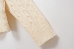 Close-up of beige cable knit sweater showing ribbed cuffs and detailed woven texture