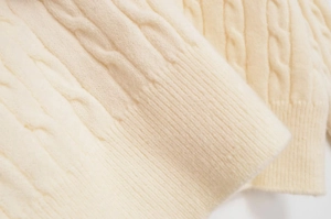 Close-up of cream cable knit sweater showing textured weave and ribbed cuffs detail