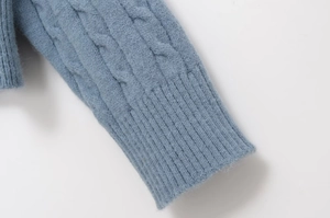 Detailed close-up of cable knit texture and ribbed cuff on a dusty blue soft sweater