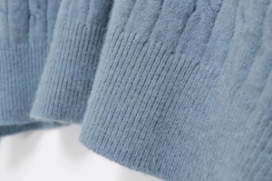 Detailed macro view of the cable knit texture and ribbed cuffs on a fuzzy blue sweater
